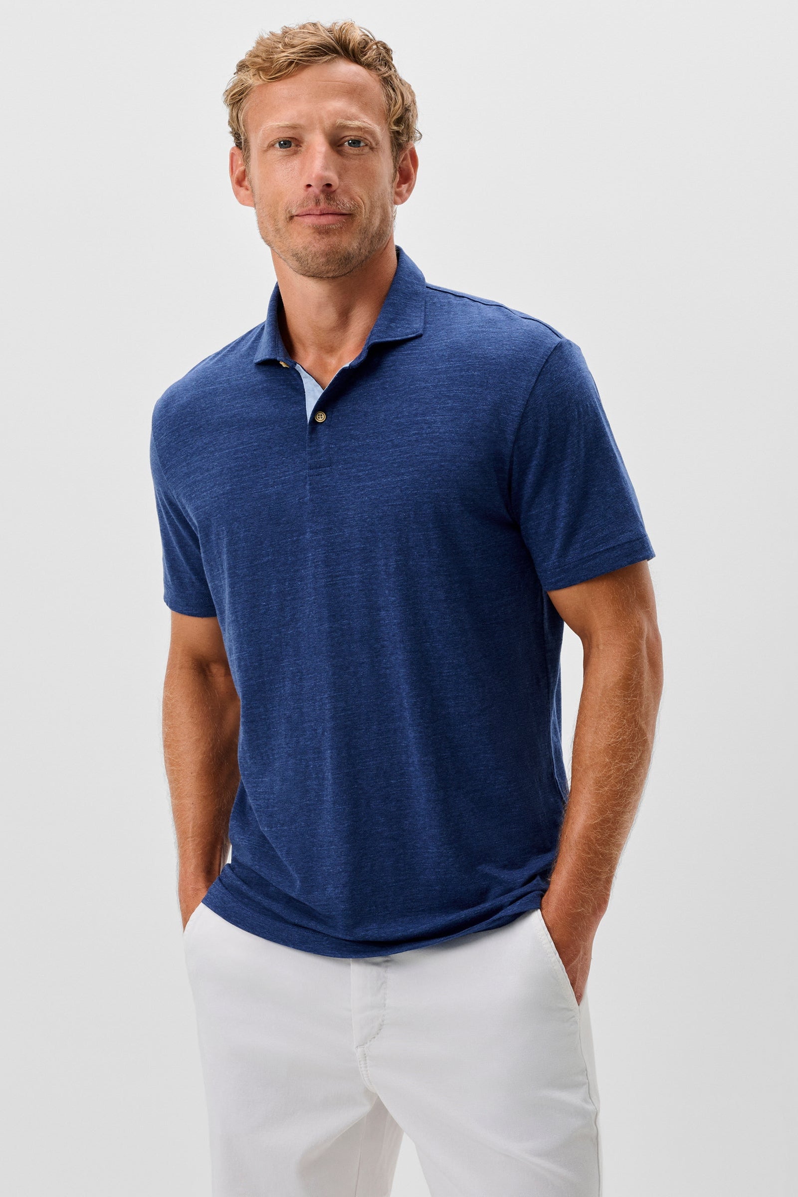 Man wearing a blue polo shirt and white pants on a light gray background