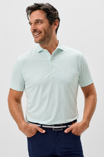 Man wearing a light green striped polo shirt and navy pants on a plain background