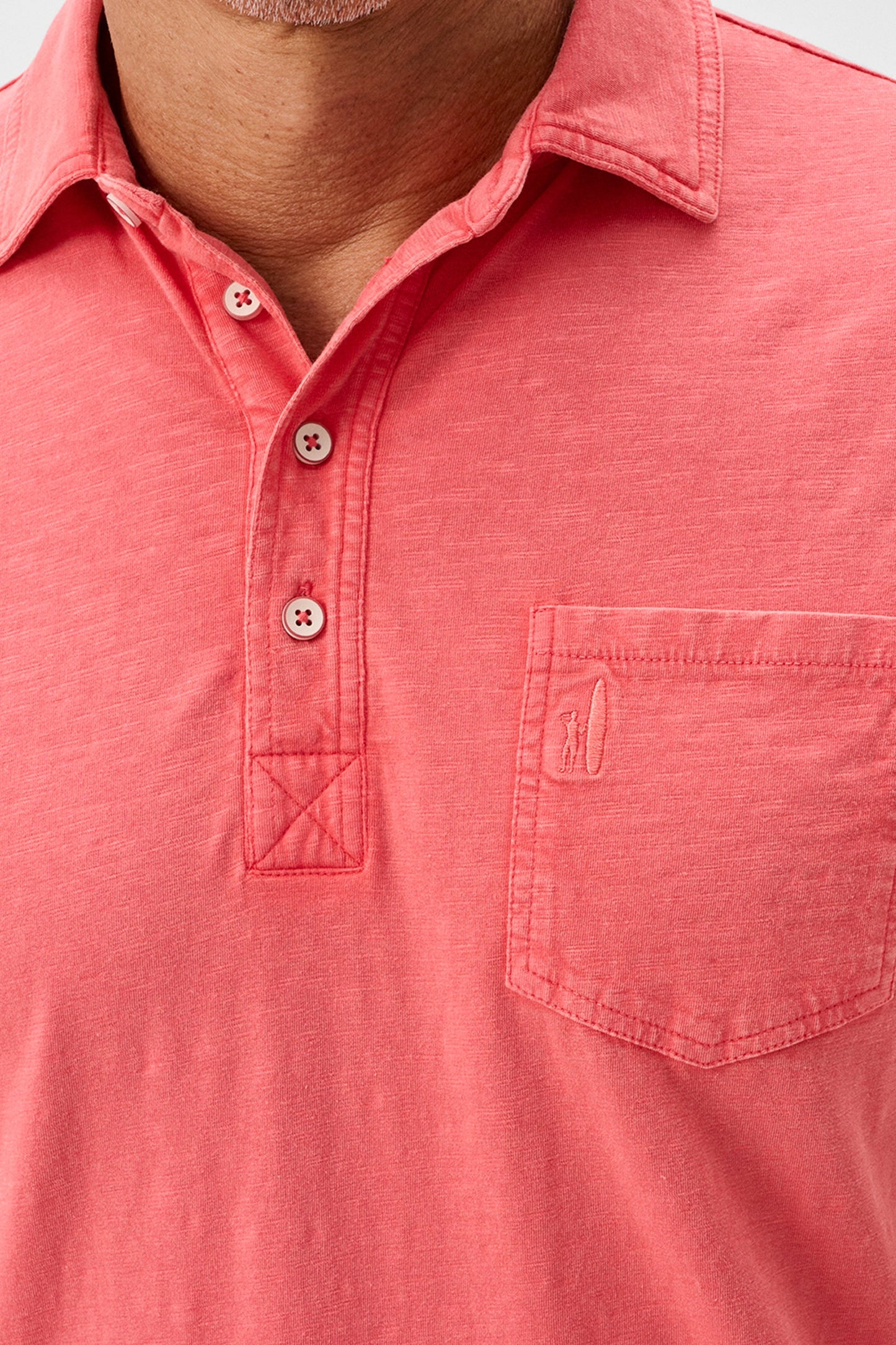 Close-up of a coral polo shirt with a pocket and buttons.