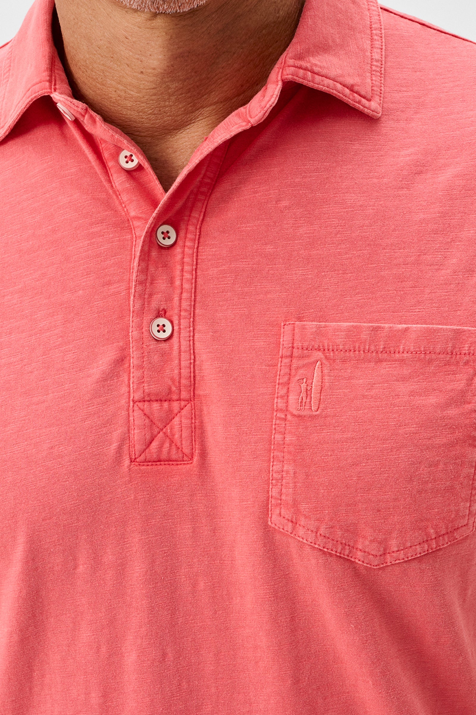 Close-up of a coral polo shirt with a pocket and buttons.
