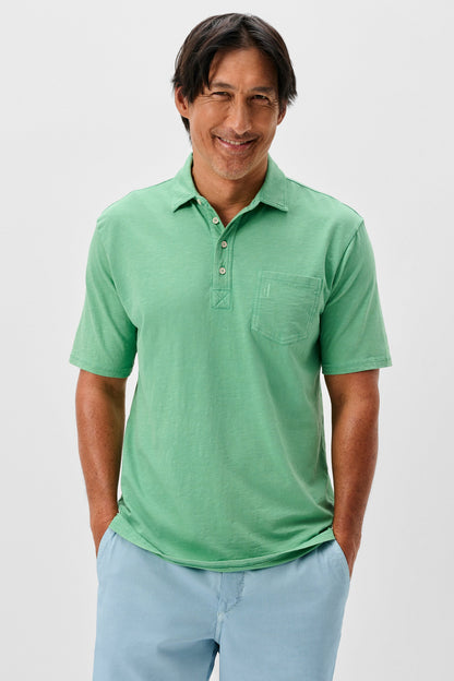 Man wearing a green polo shirt and light blue pants on a plain background