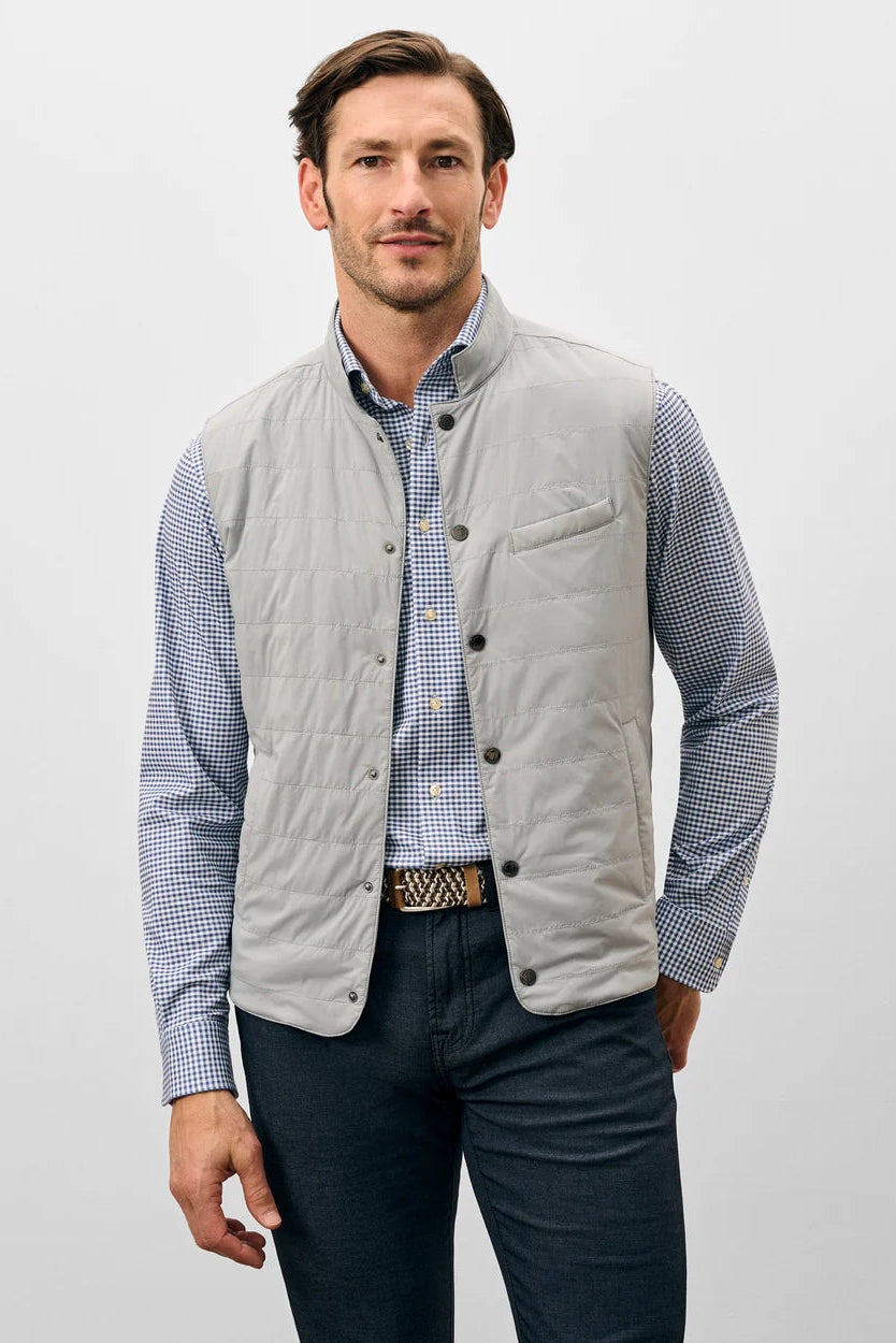 Man wearing a light gray quilted vest over a checkered shirt on a white background