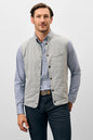 Man wearing a light gray quilted vest over a checkered shirt on a white background