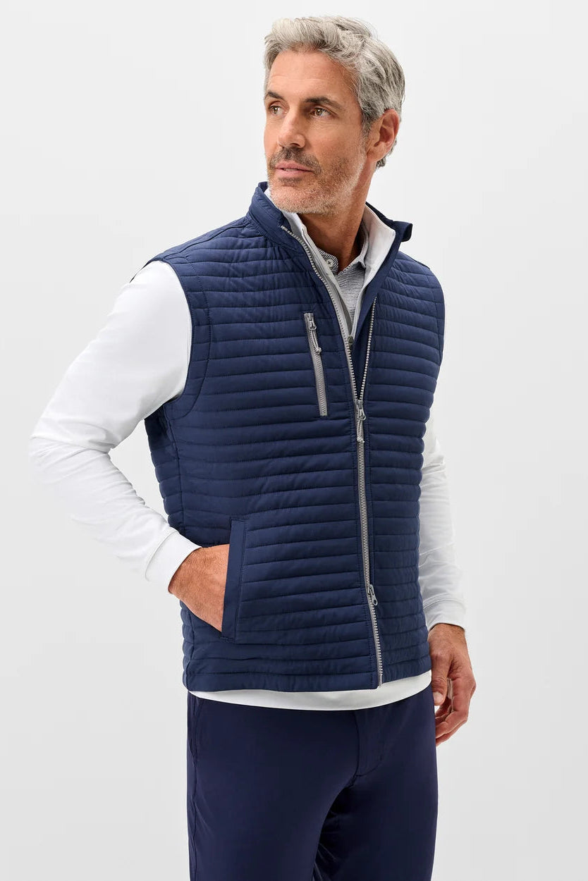 Man wearing a navy puffer vest with a logo on a light gray background