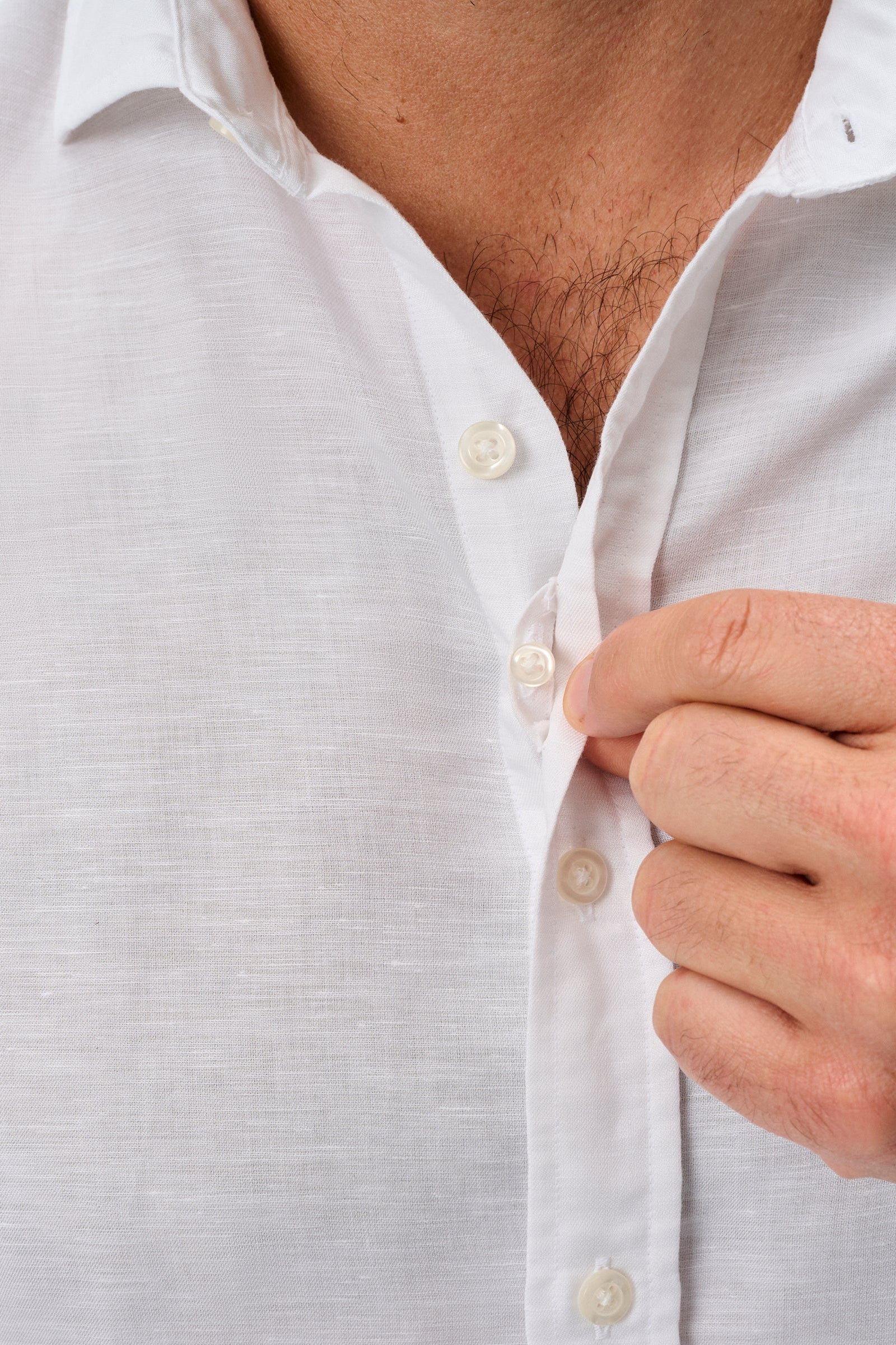 Close-up of a person buttoning a white shirt against a light gray background