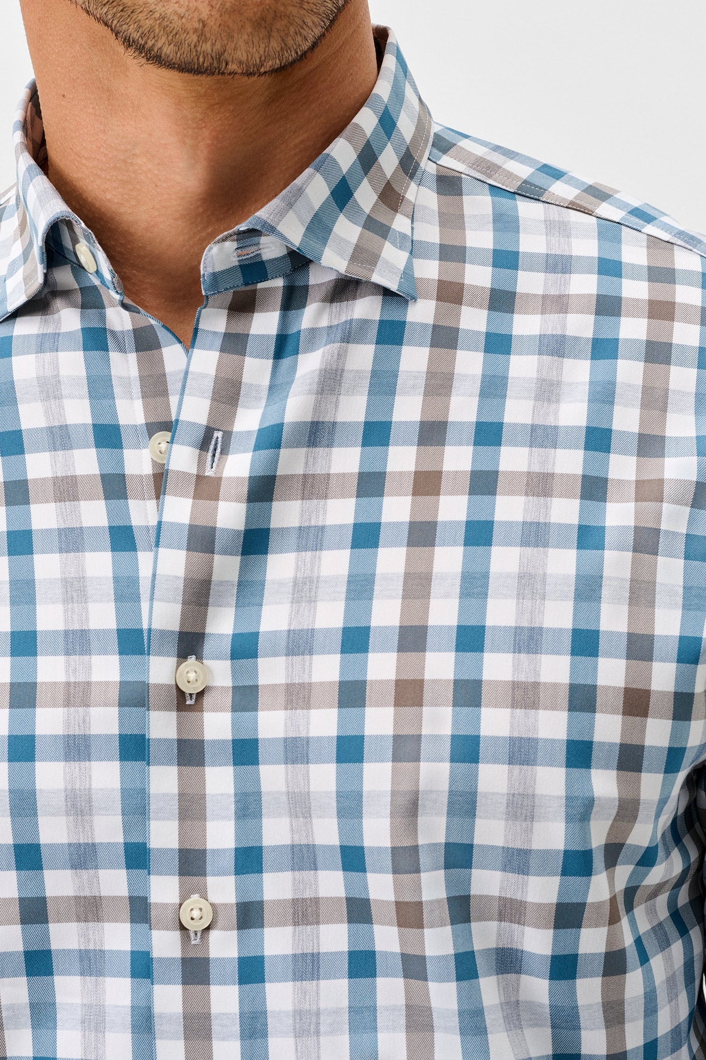 A close-up of a man wearing a long-sleeve button-down shirt with a blue, gray, and white checkered pattern.