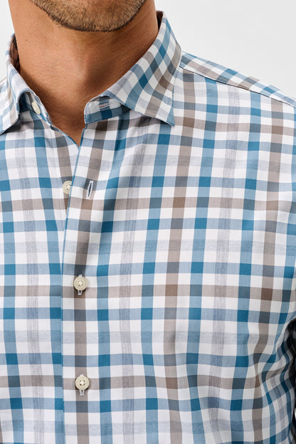 A close-up of a man wearing a long-sleeve button-down shirt with a blue, gray, and white checkered pattern.