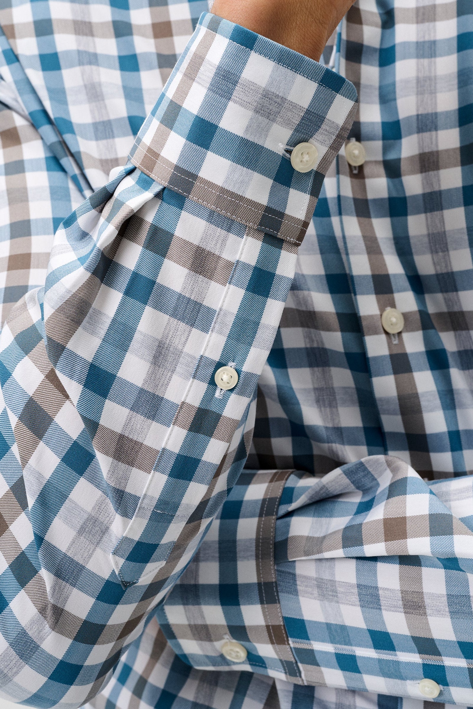 Close-up of a men's long-sleeve button-down shirt with a blue, white, and brown gingham check pattern, showing the cuff and buttons.