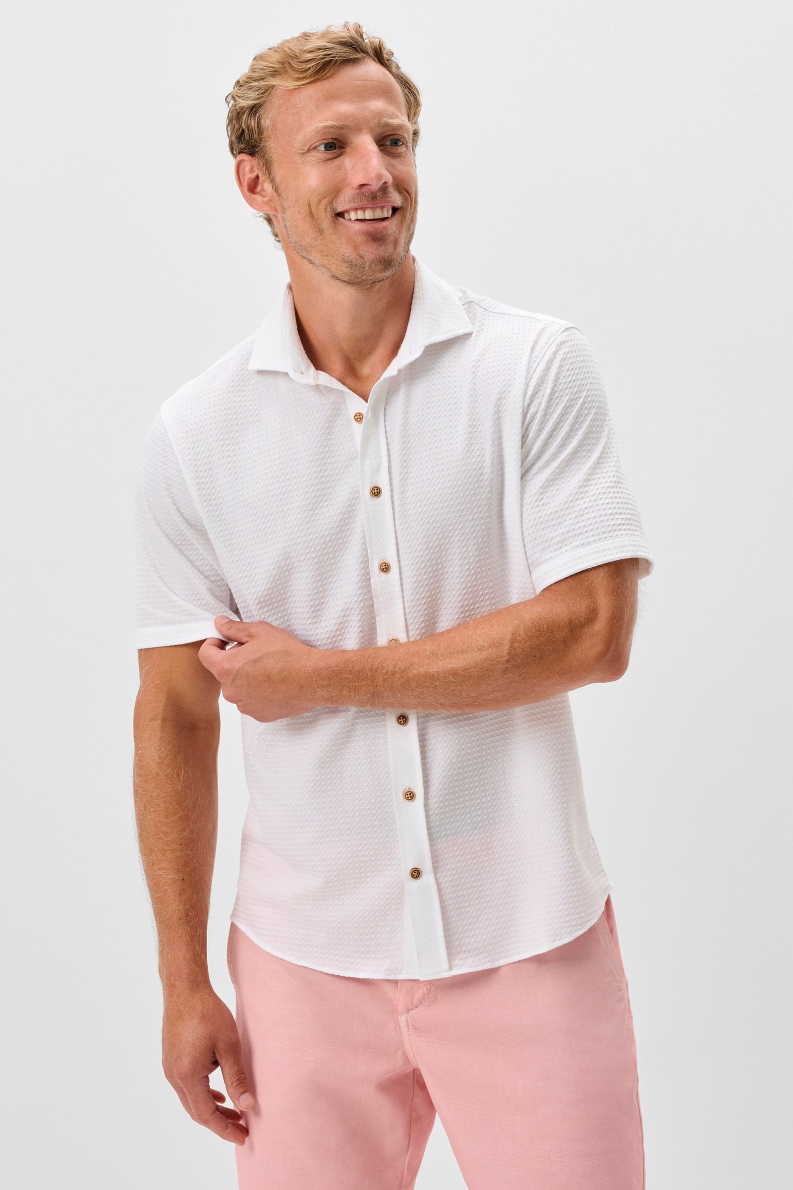 Man wearing a white short-sleeve shirt and pink pants on a light gray background