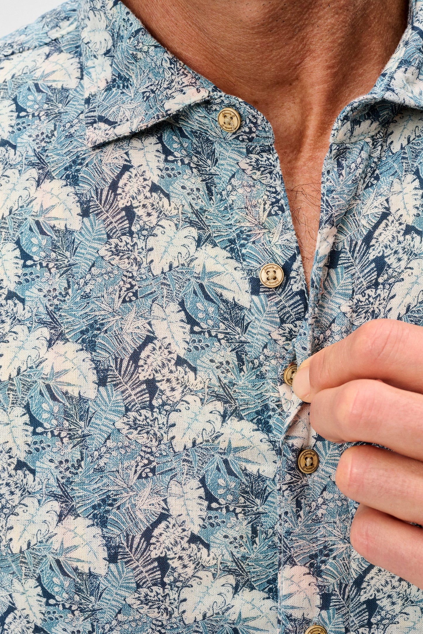 Close-up of a person wearing a blue floral shirt with a button being adjusted.