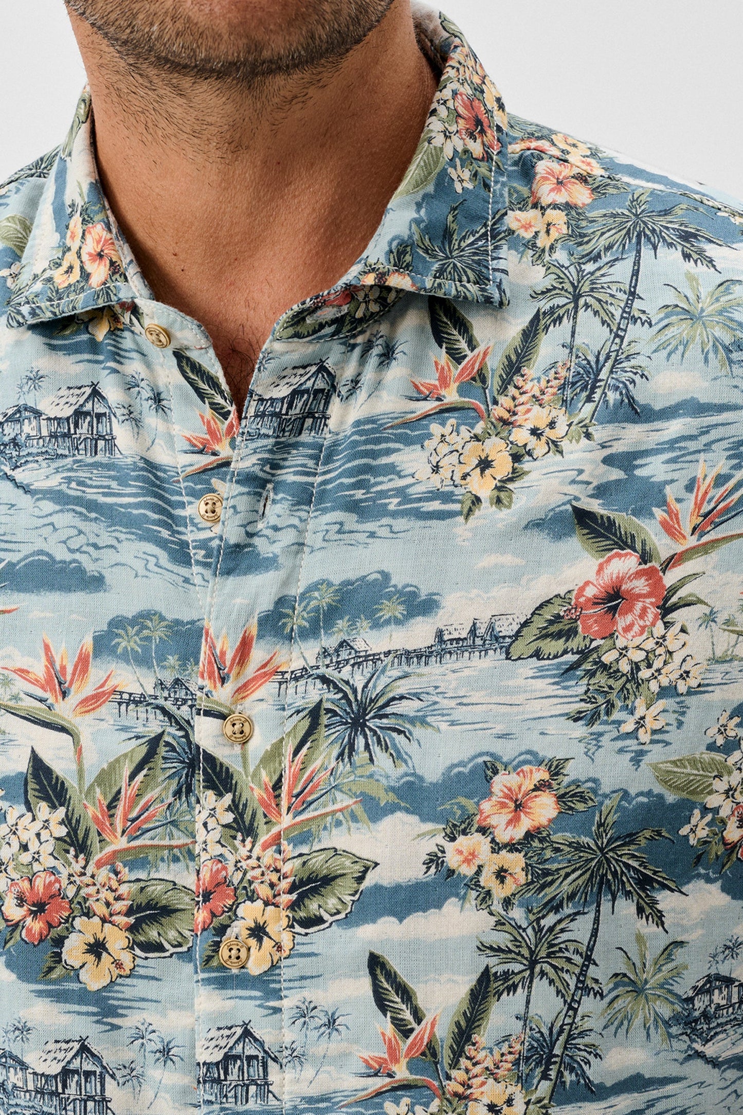 Hawaiian shirt with tropical design featuring flowers and palm trees on a blue background.