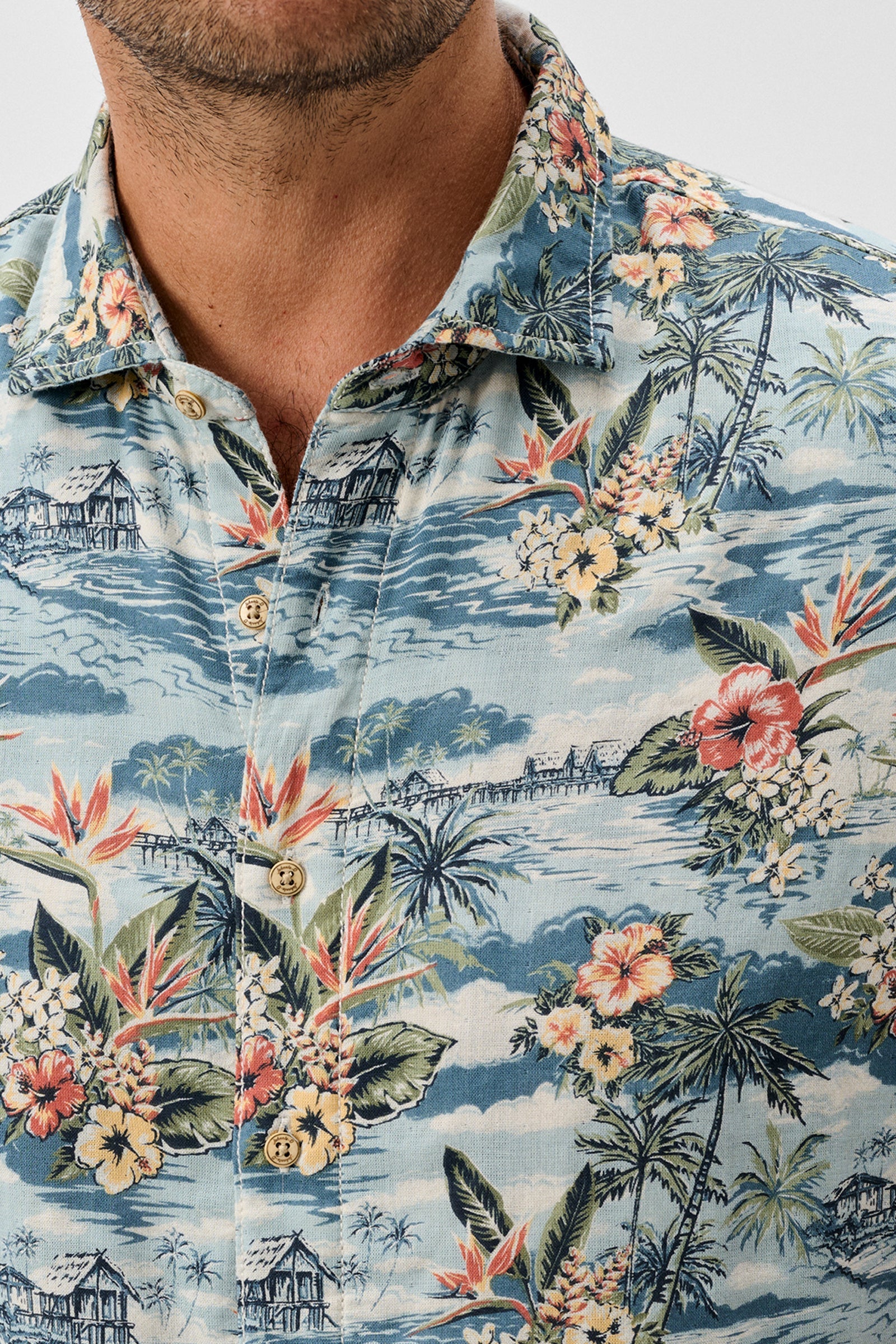 Hawaiian shirt with tropical design featuring flowers and palm trees on a blue background.