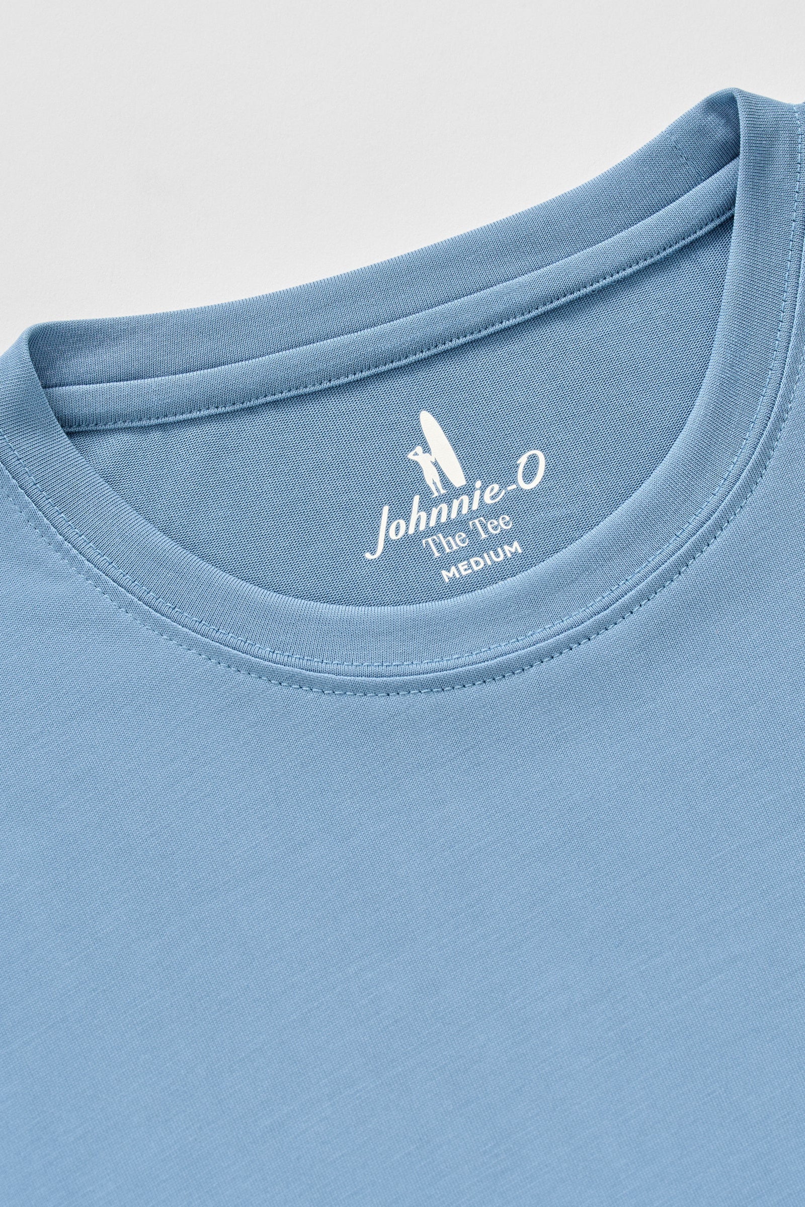Close-up of a blue t-shirt with a brand logo on the collar against a light gray background