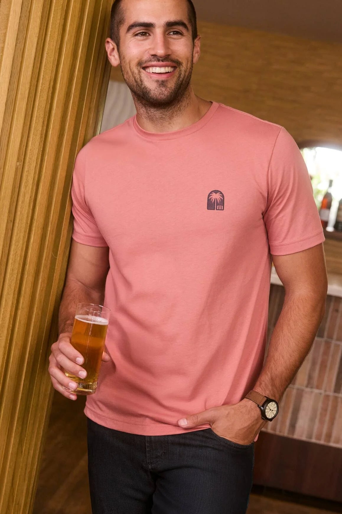 Man in a pink t-shirt holding a beer in a casual setting