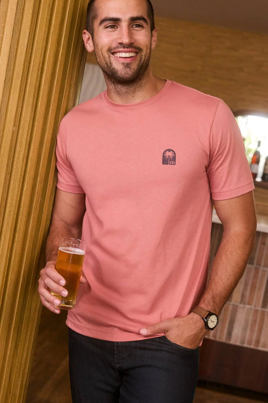 Man in a pink t-shirt holding a beer in a casual setting