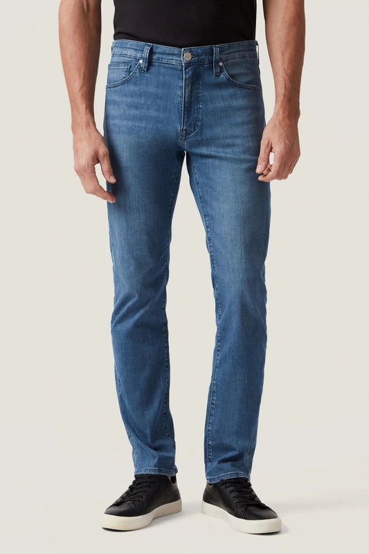 Person wearing blue jeans and black shoes on a plain background