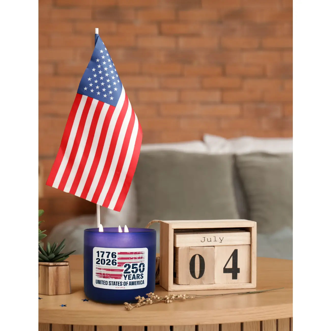 Blue candle with American flag and '250 Years' label on a wooden surface with a brick wall background.