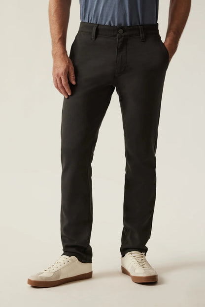 A person wearing slim-fit black chinos with a blue shirt and white sneakers, shown from the waist down against a light beige studio background.