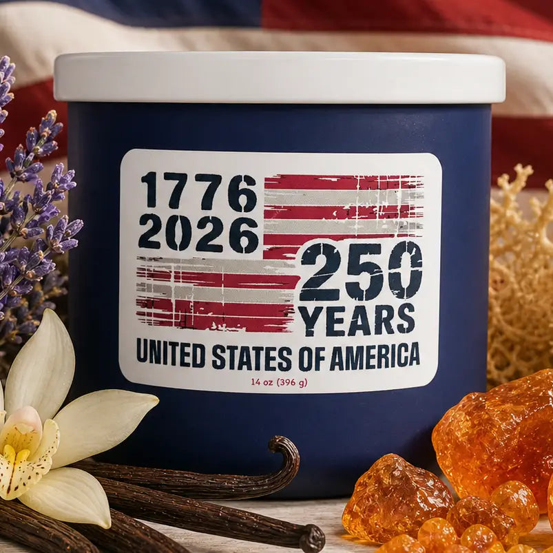 Navy blue candle with a label celebrating 250 years of the United States of America, surrounded by vanilla beans and flowers.