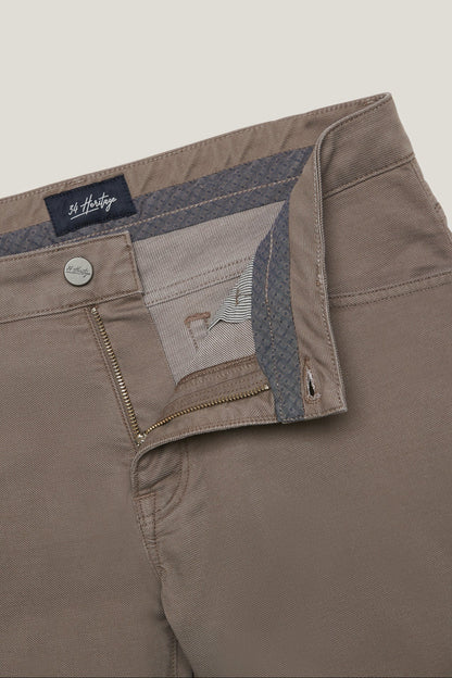 Close-up of a pair of St. Hilda men's trousers in a taupe-brown color, showing the interior waistband with a patterned lining, a silver metal button, and a zippered pocket.