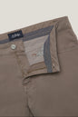 Close-up of a pair of St. Hilda men's trousers in a taupe-brown color, showing the interior waistband with a patterned lining, a silver metal button, and a zippered pocket.