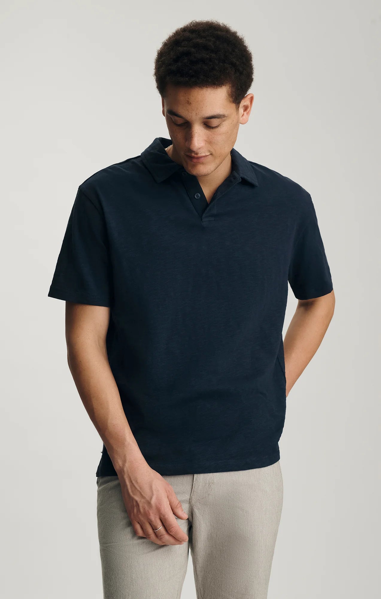 Man wearing a navy polo shirt and light gray pants on a plain background
