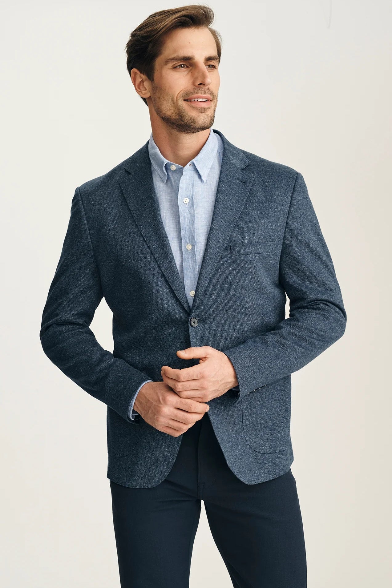 Man wearing a blue blazer over a light blue shirt on a plain background