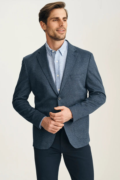Man wearing a blue blazer over a light blue shirt on a plain background