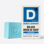 Blue bar of soap next to its packaging with 'Duke Cannon' branding on a white background.