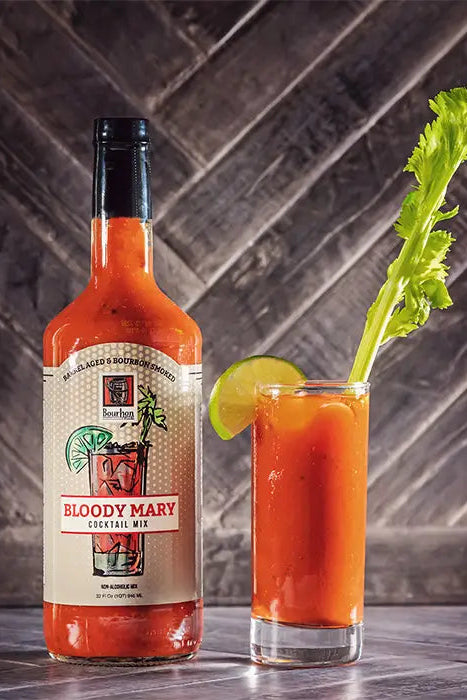 Bottle of Bloody Mary mix and a glass of Bloody Mary with celery and lime on a wooden surface.