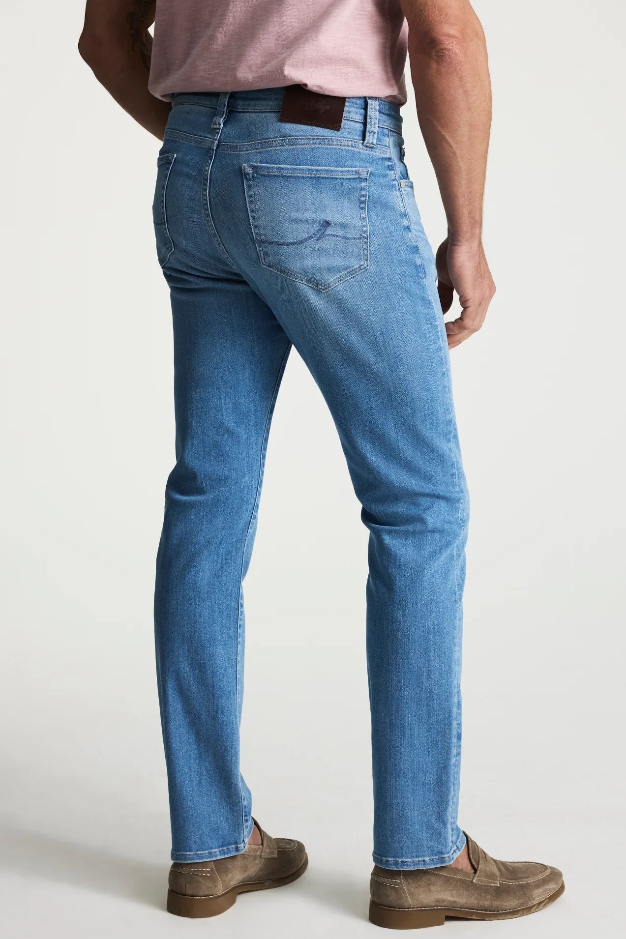Person wearing blue jeans and brown shoes on a white background