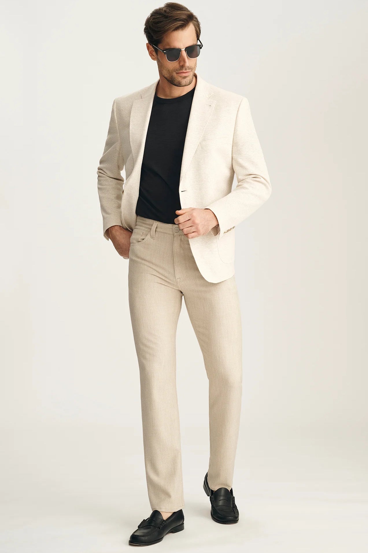 Man wearing a beige suit with black shirt and shoes on a white background