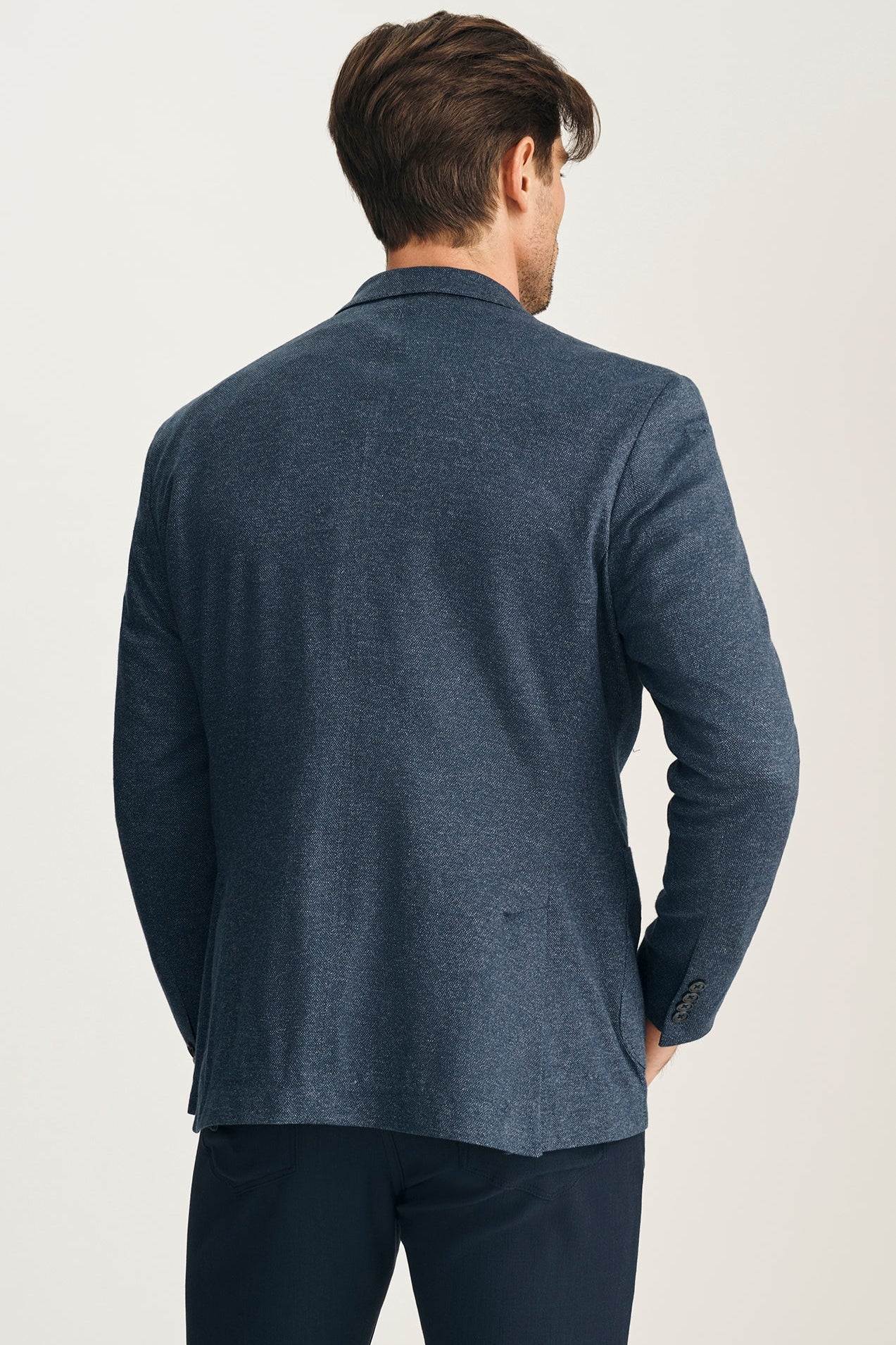 Man wearing a blue blazer from behind on a light background