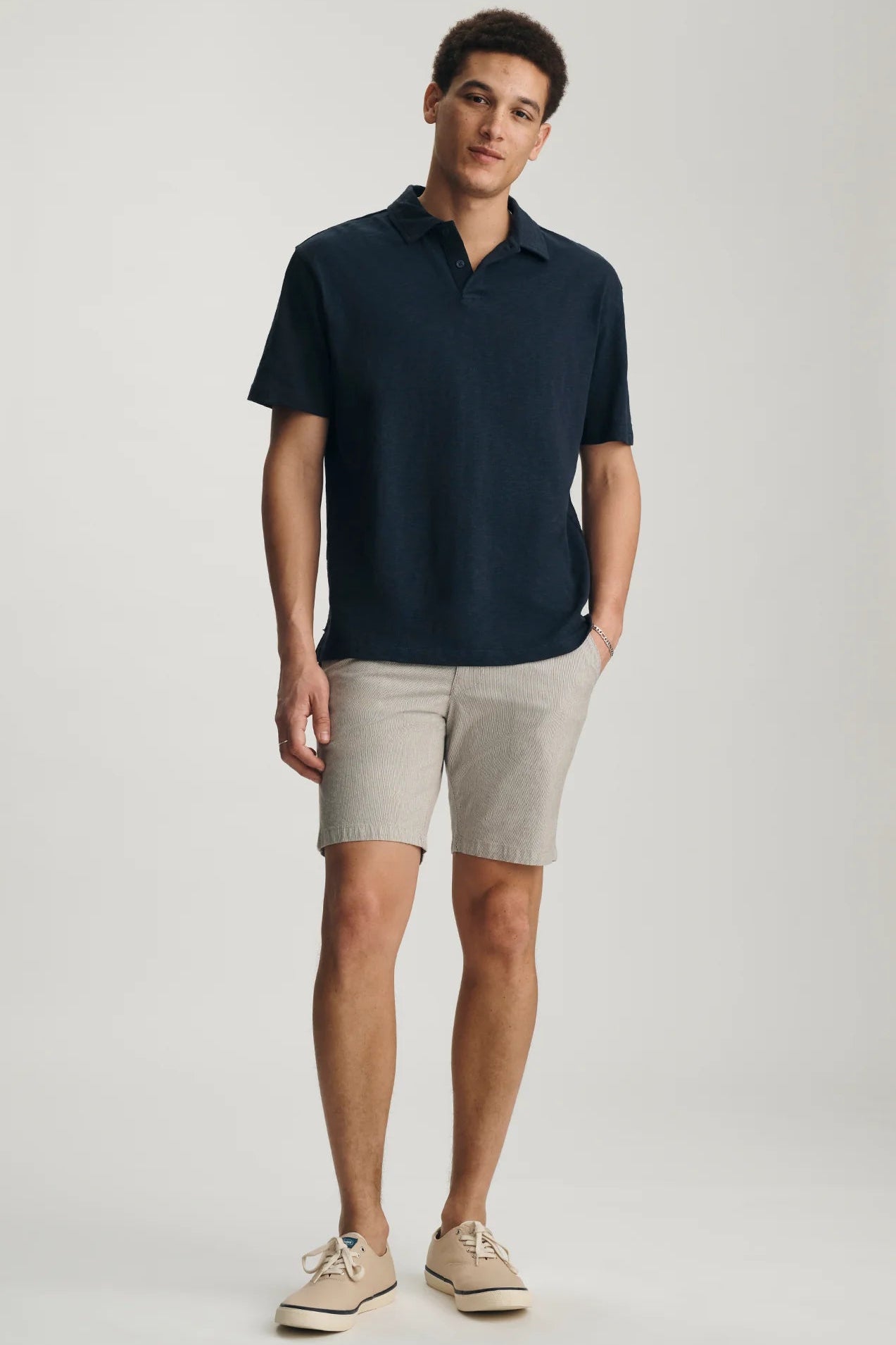 Man wearing a navy polo shirt and beige shorts on a white background