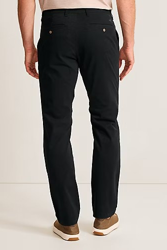 Rear view of a person wearing slim black trousers with brown shoes, shown against a plain light studio background.
