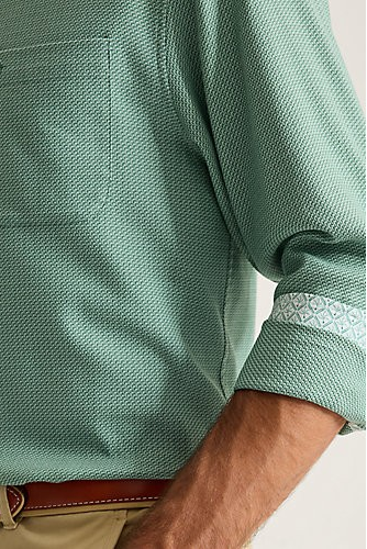 Close-up of a man wearing a mint green textured long-sleeve button-down shirt with a chest pocket and rolled-up cuffs, paired with khaki pants and a brown belt.