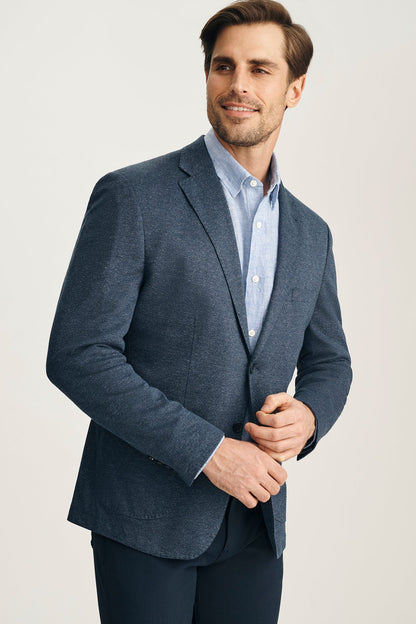 Man wearing a blue blazer over a light blue shirt on a plain background