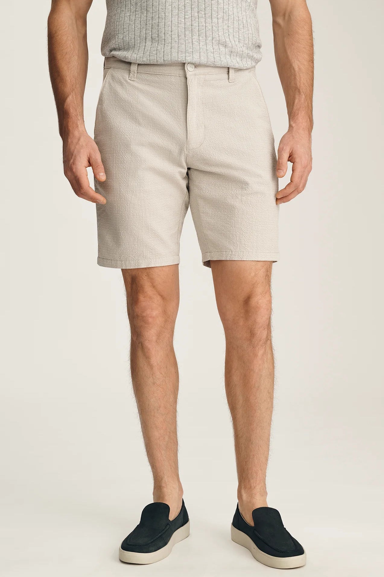 Person wearing beige shorts and black shoes on a plain background