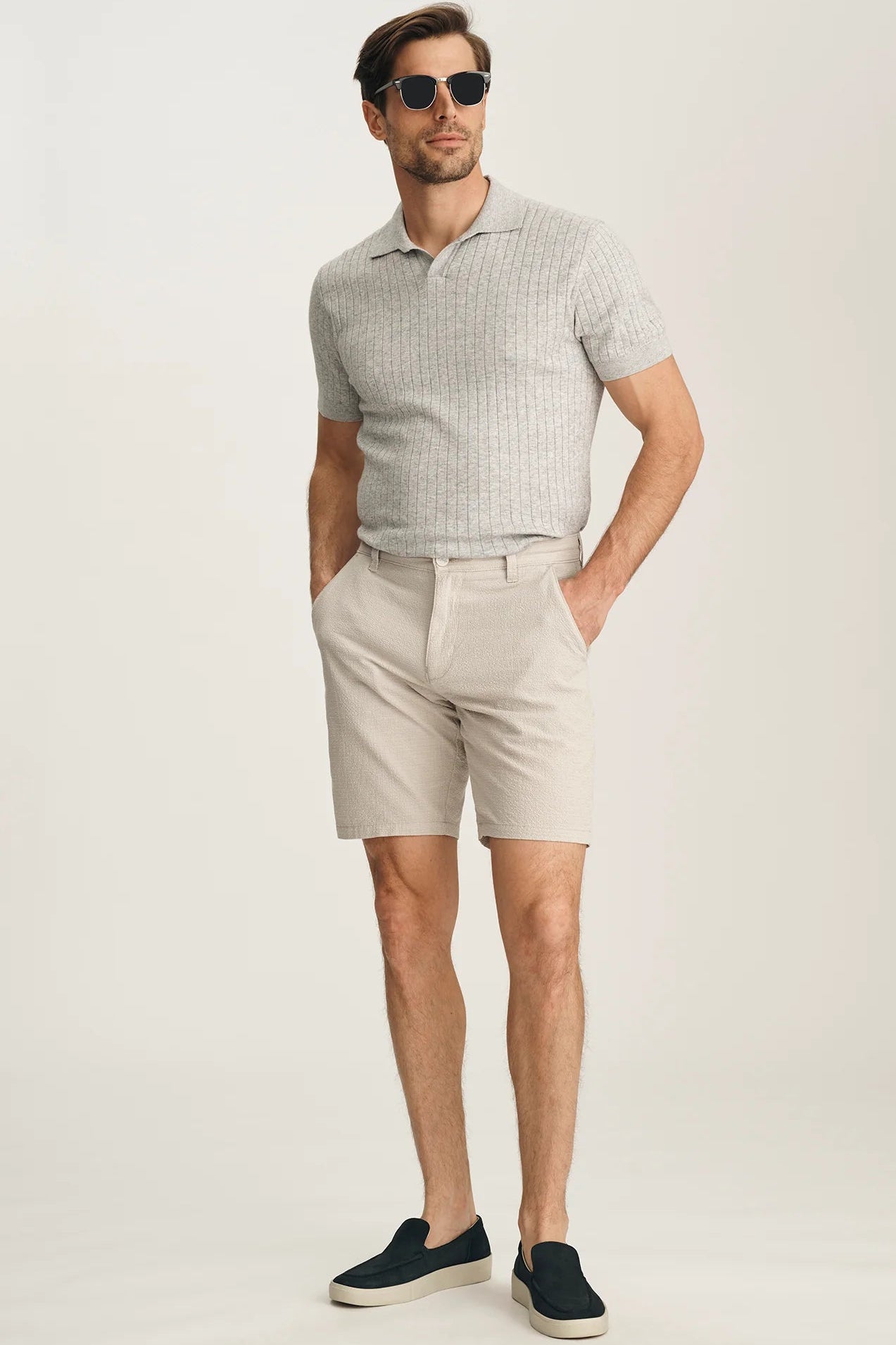 Man wearing a light gray polo shirt and beige shorts on a white background