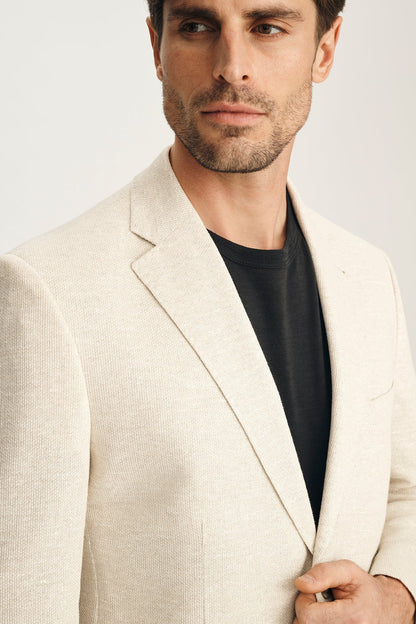 Man wearing a beige blazer over a black shirt on a light gray background