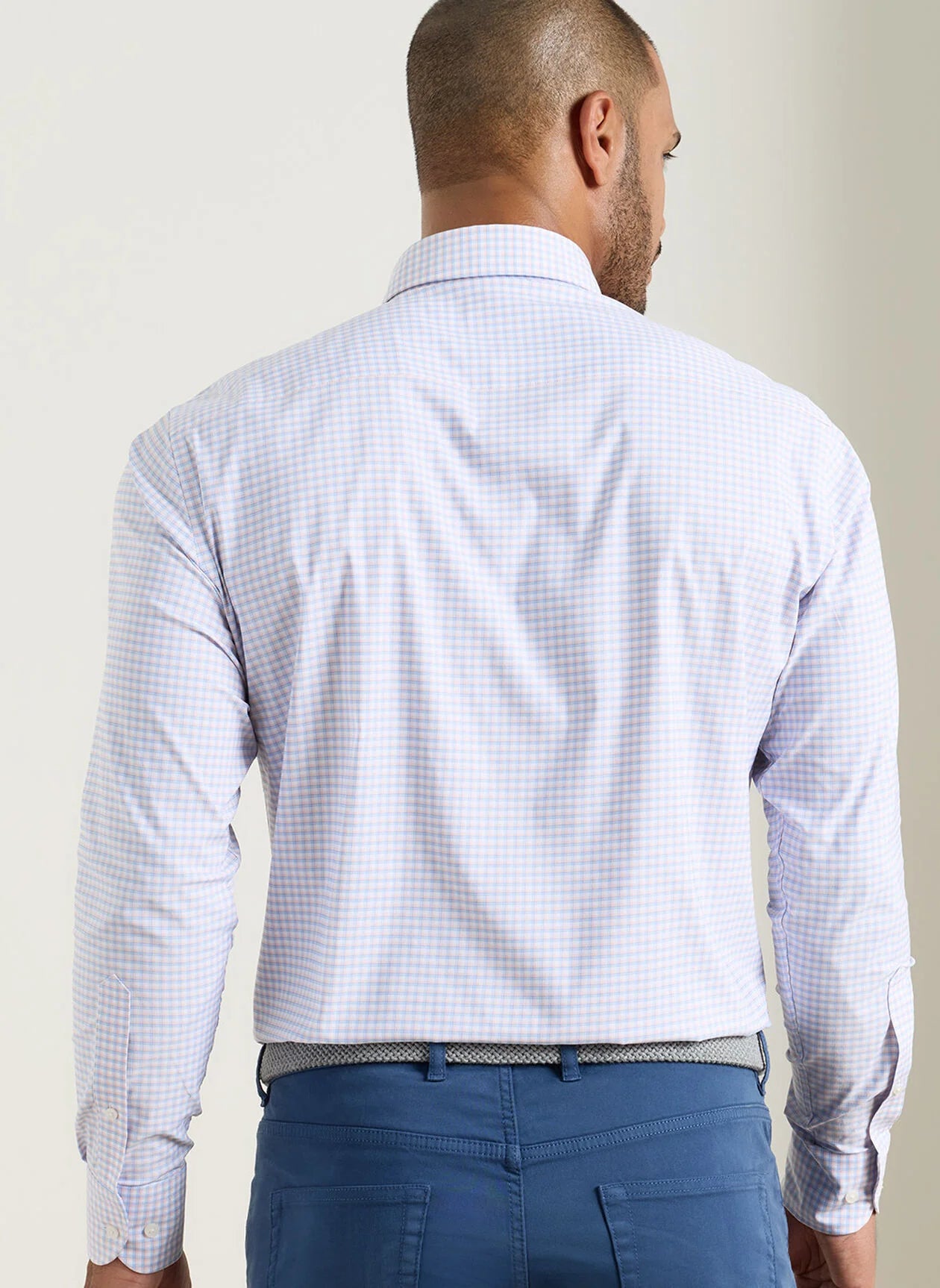 Man wearing a light blue checkered shirt and blue pants against a plain background