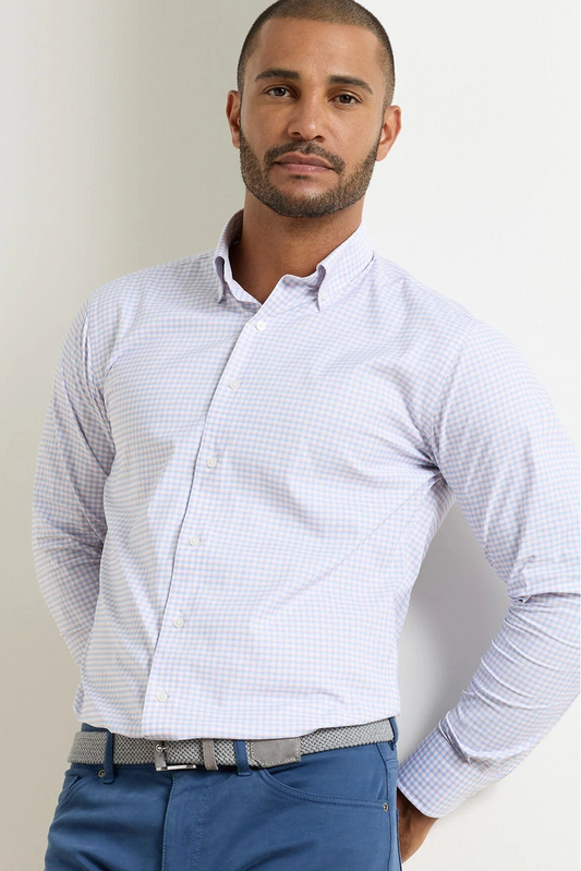 A man wearing a light blue and white micro-checkered long-sleeve button-down shirt, paired with blue trousers and a gray patterned belt, standing against a plain off-white background.