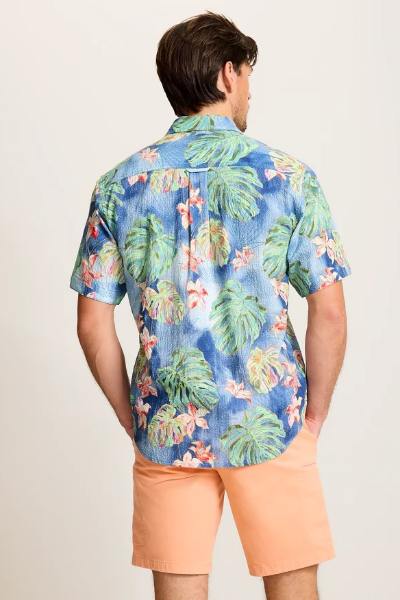 Man wearing a tropical patterned shirt and peach shorts on a plain background