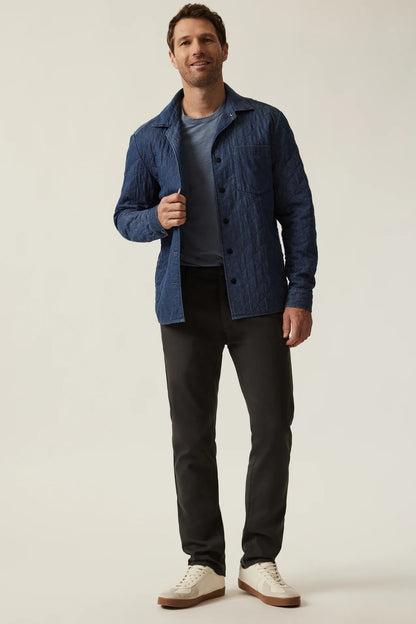 A man modeling a textured blue button-up overshirt over a dark gray t-shirt, black trousers, and off-white sneakers, photographed against a neutral light gray studio background.