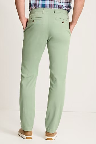 A person shown from the back wearing light sage green slim-fit chinos with a plaid shirt and tan shoes, photographed against a clean off-white studio background.