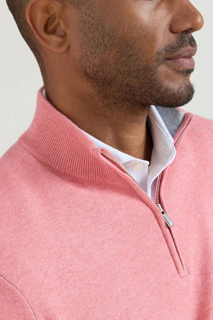 A close-up side profile of a man wearing a pink quarter-zip mock neck sweater over a white collared shirt, against a light neutral background.