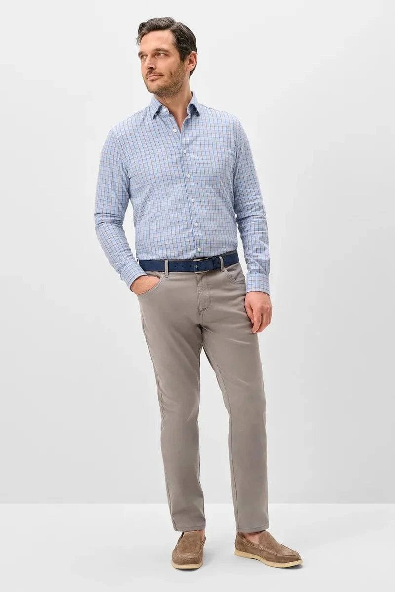 A man modeling a light blue and white checkered long-sleeve button-down shirt, paired with taupe trousers, a dark blue belt, and brown suede shoes, against a plain light gray studio background.