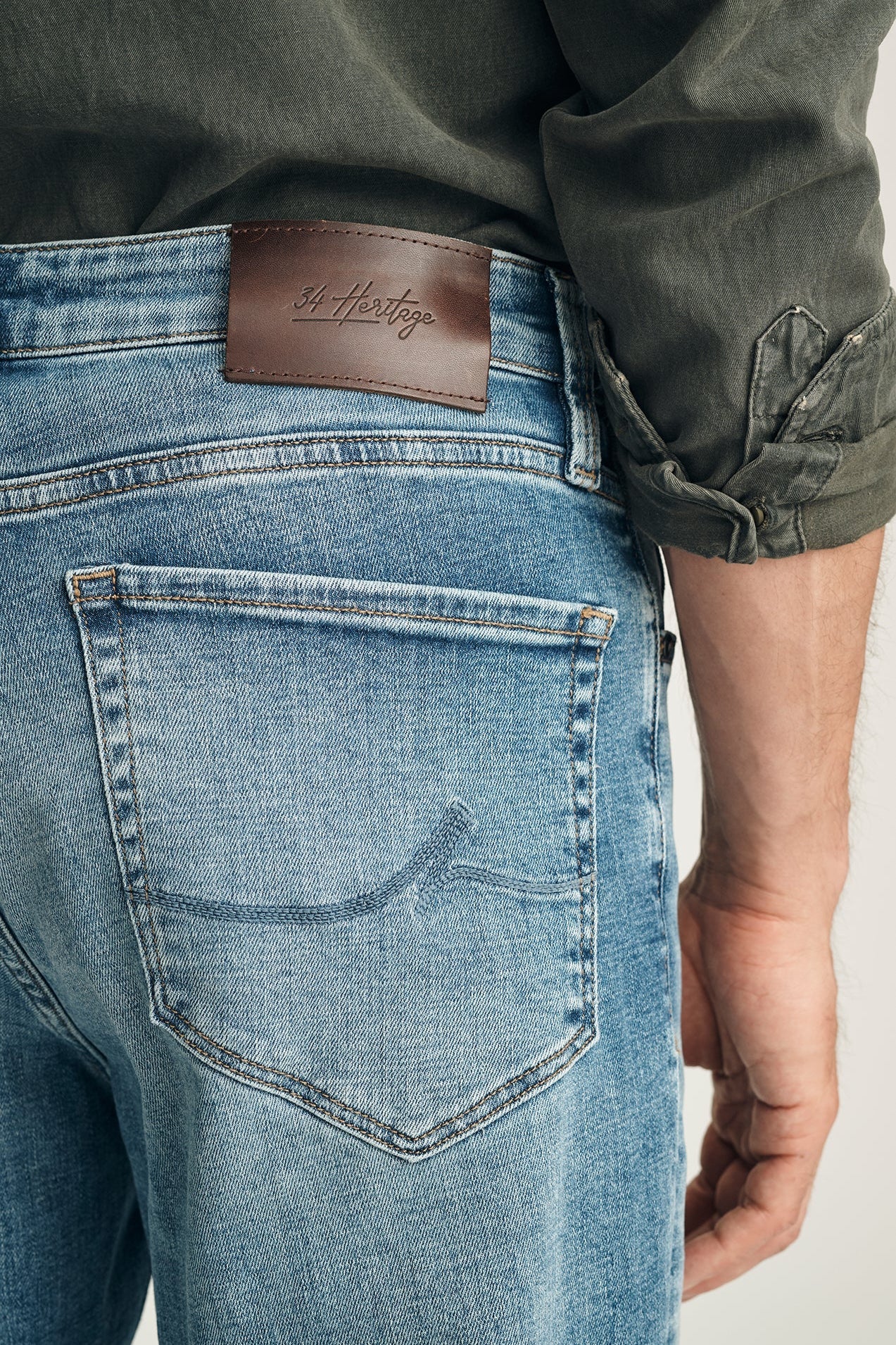 Close-up of blue jeans with a brand label on the back pocket, worn by a person.