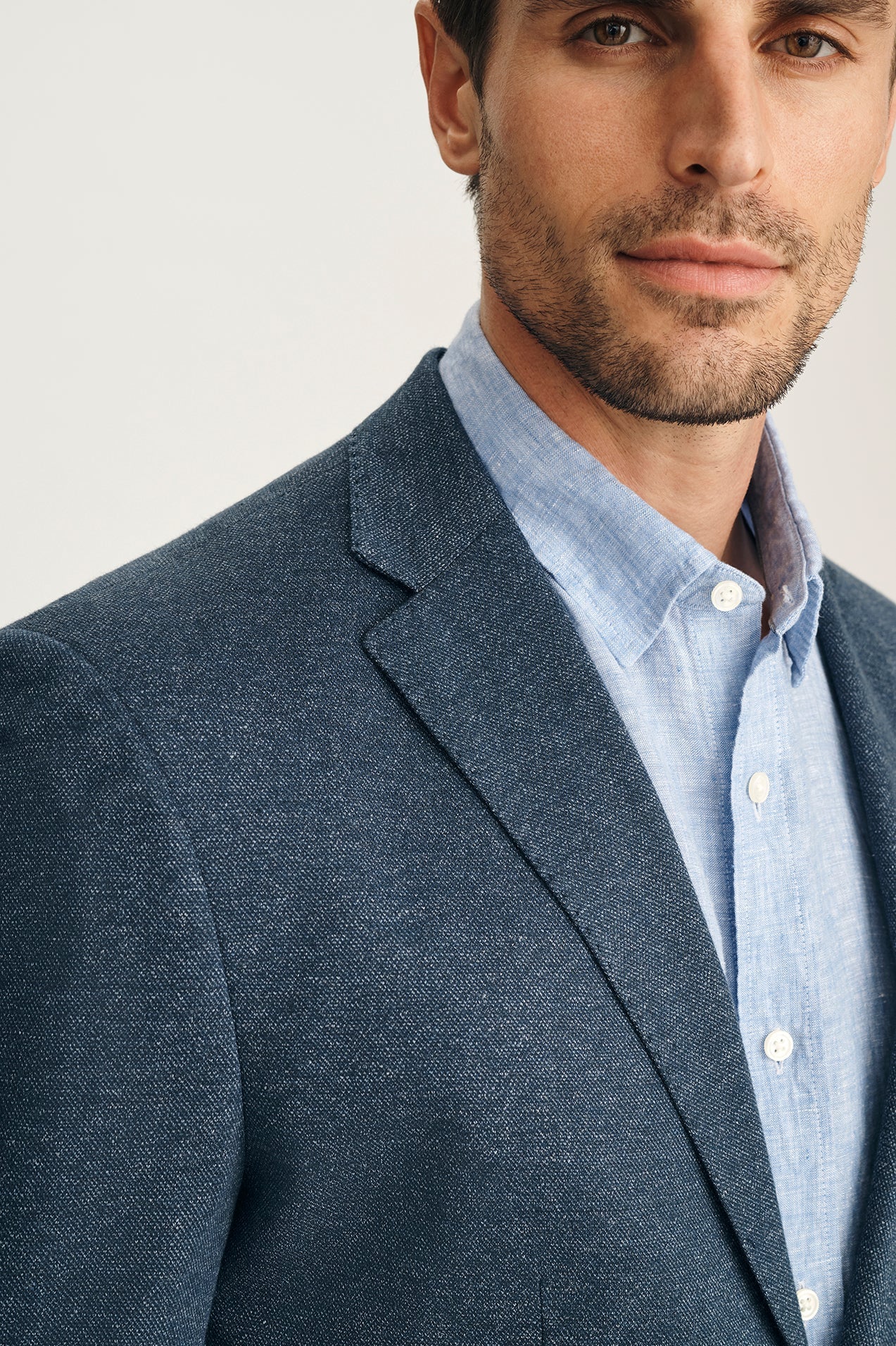 Man wearing a dark gray blazer over a light blue shirt with a white collar.