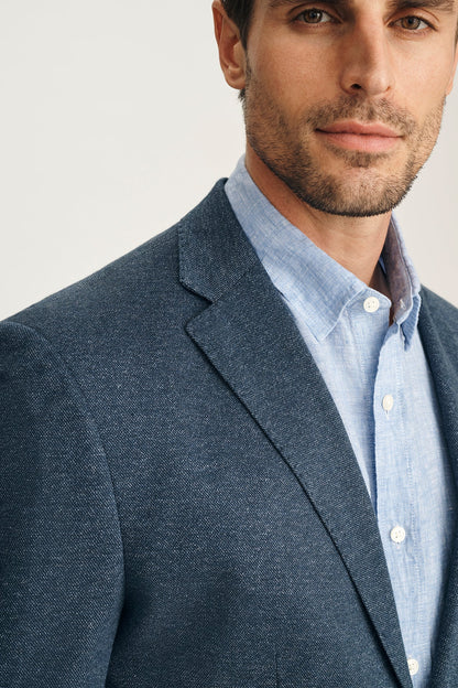 Man wearing a dark gray blazer over a light blue shirt with a white collar.